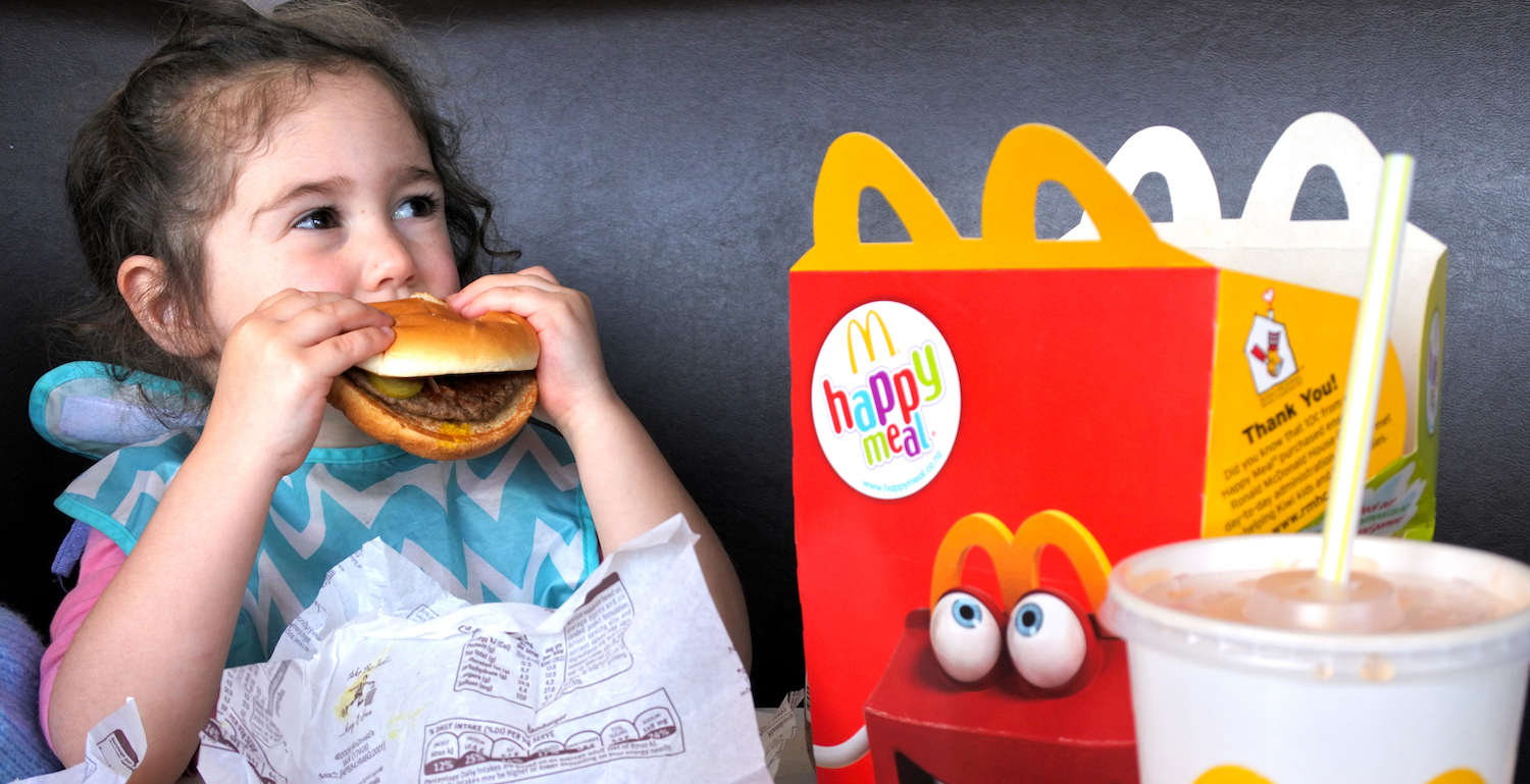 AUCKLAND - NOV 12 2017:Small girl (Naomi Ben-Ari age 03) eats fast food. Fast food is highly processed and contains large amounts of carbohydrates, added sugar, unhealthy fats, and salt (sodium).